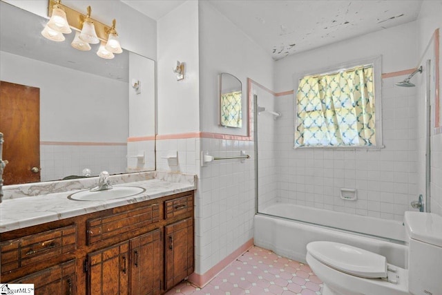 bathroom featuring toilet, a wainscoted wall,  shower combination, vanity, and tile walls