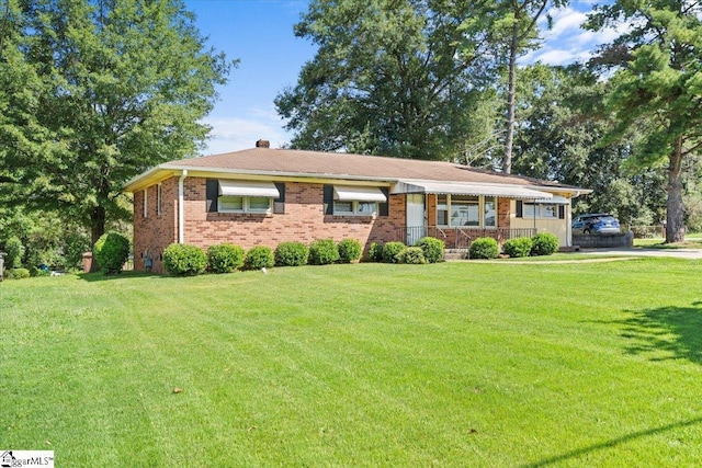 single story home featuring brick siding, a chimney, and a front yard