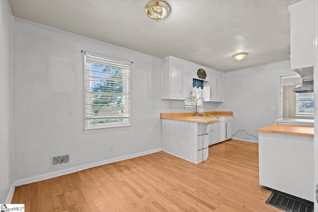 kitchen with kitchen peninsula, white cabinets, light wood-type flooring, and sink