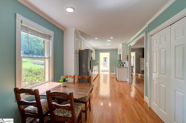 dining area featuring light wood-type flooring, crown molding, and a textured ceiling