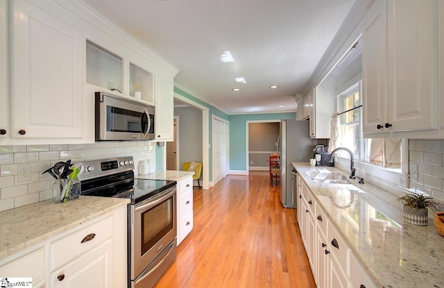 kitchen featuring white cabinetry, light wood-type flooring, light stone countertops, ornamental molding, and appliances with stainless steel finishes