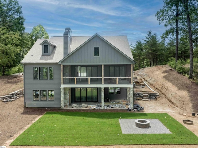 rear view of house with a sunroom, a patio, a yard, and a fire pit