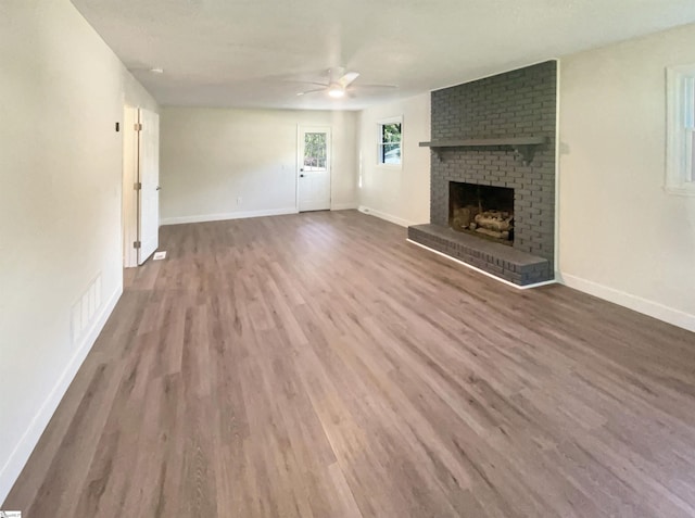 unfurnished living room with a brick fireplace, visible vents, baseboards, and wood finished floors