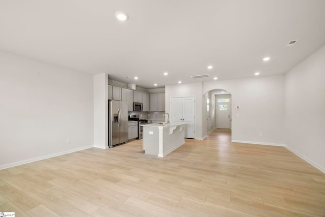 kitchen with appliances with stainless steel finishes, light hardwood / wood-style flooring, sink, a kitchen island with sink, and gray cabinets