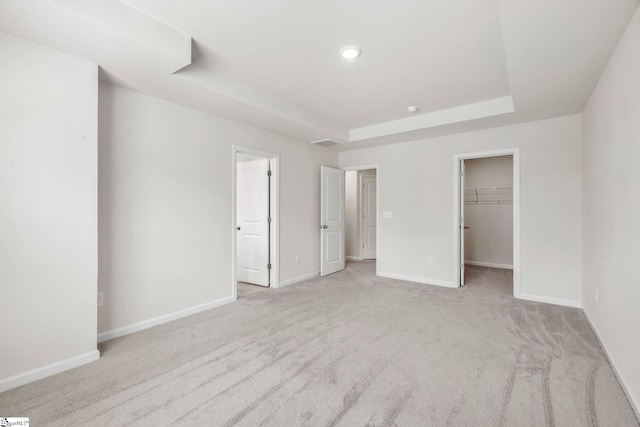 unfurnished bedroom with a closet, a raised ceiling, a spacious closet, and light colored carpet