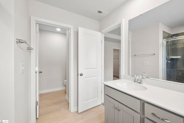 bathroom featuring wood-type flooring, a shower with door, toilet, and vanity