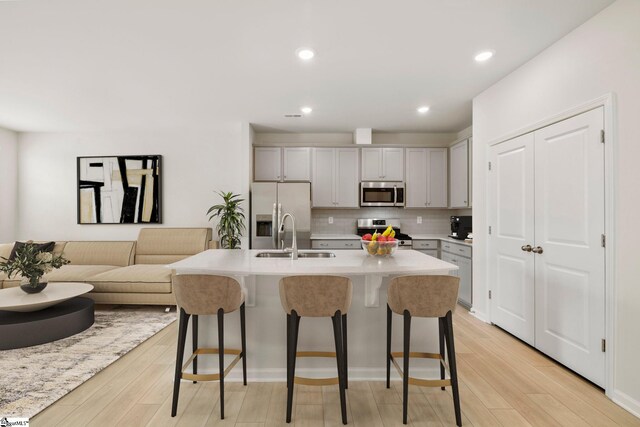 kitchen with gray cabinets, tasteful backsplash, a kitchen island with sink, sink, and stainless steel appliances