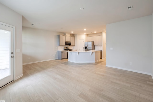 kitchen with a breakfast bar, appliances with stainless steel finishes, an island with sink, and light hardwood / wood-style floors