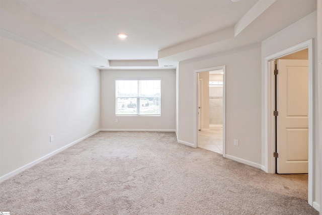 unfurnished bedroom featuring a raised ceiling, light carpet, and ensuite bath