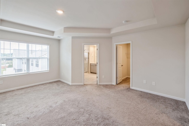 unfurnished bedroom featuring ensuite bath, a closet, a spacious closet, light carpet, and a tray ceiling