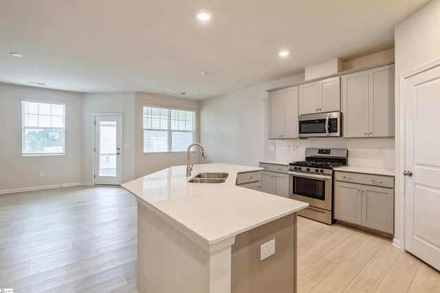 kitchen featuring sink, appliances with stainless steel finishes, light hardwood / wood-style flooring, gray cabinetry, and a center island with sink