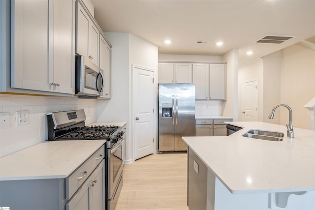 kitchen featuring appliances with stainless steel finishes, decorative backsplash, sink, light stone counters, and light wood-type flooring