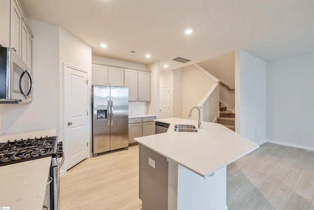 kitchen with sink, appliances with stainless steel finishes, light hardwood / wood-style floors, a kitchen island with sink, and tasteful backsplash