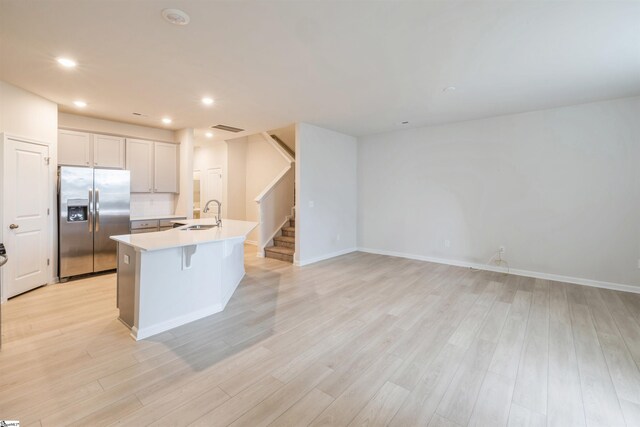 kitchen with a kitchen bar, sink, light wood-type flooring, stainless steel refrigerator with ice dispenser, and a center island with sink