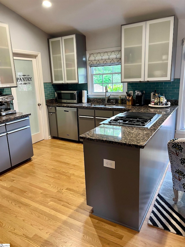 kitchen with tasteful backsplash, light wood-type flooring, appliances with stainless steel finishes, dark stone countertops, and vaulted ceiling