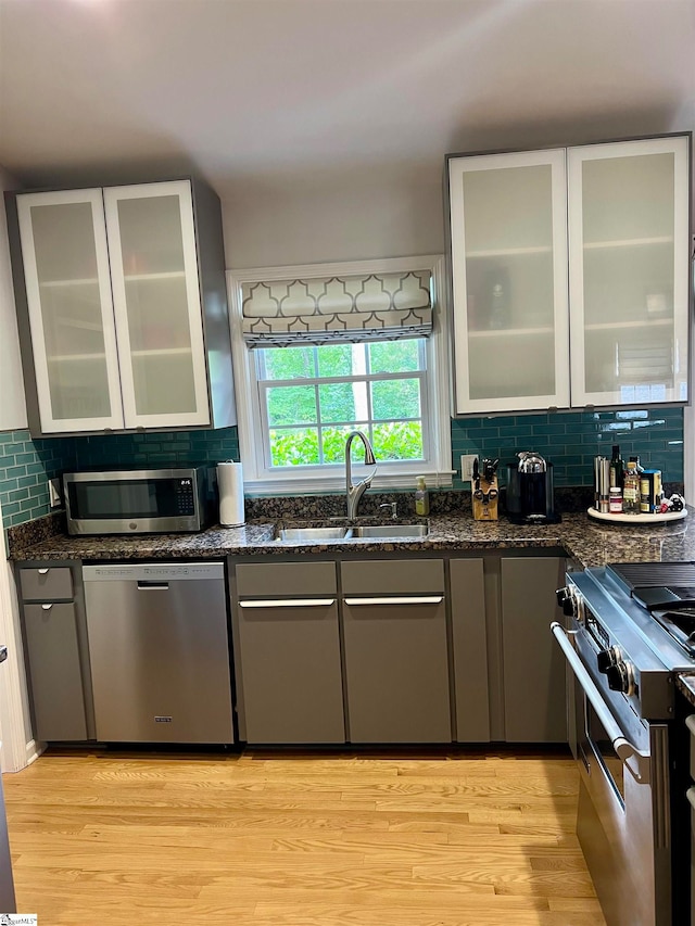 kitchen with dark stone countertops, stainless steel appliances, decorative backsplash, light wood-type flooring, and sink