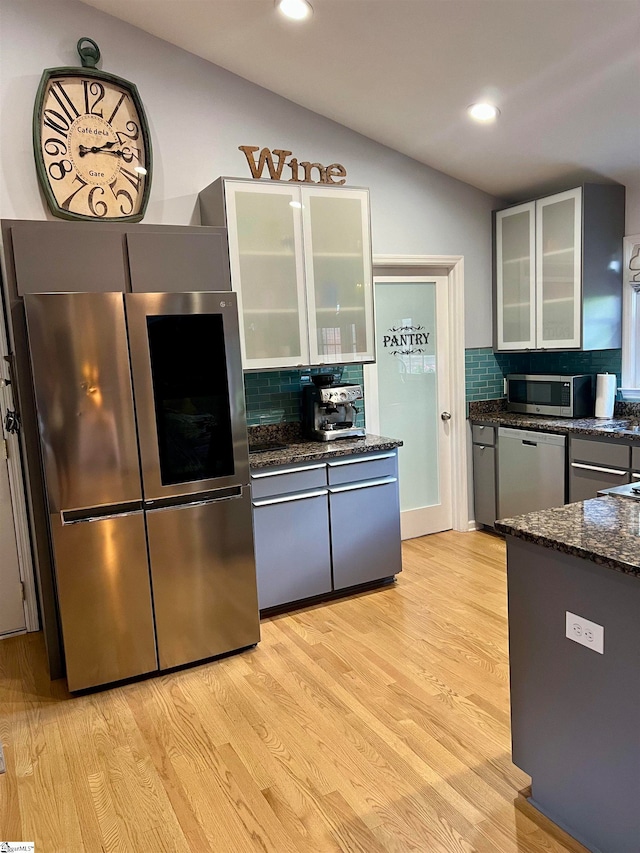 kitchen featuring stainless steel appliances, dark stone countertops, light hardwood / wood-style flooring, decorative backsplash, and vaulted ceiling