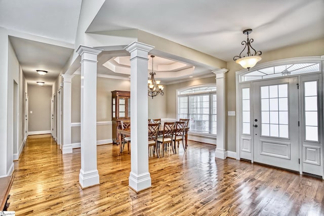 foyer entrance with an inviting chandelier, crown molding, ornate columns, a tray ceiling, and hardwood / wood-style floors