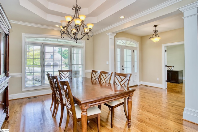 dining room with crown molding, ornate columns, light hardwood / wood-style floors, a raised ceiling, and a chandelier