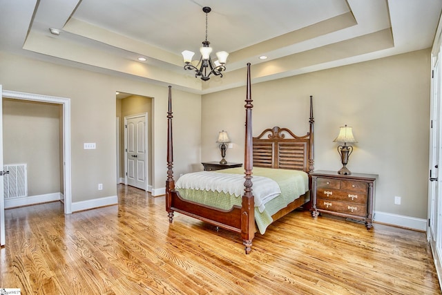 bedroom with a notable chandelier, a raised ceiling, and light wood-type flooring