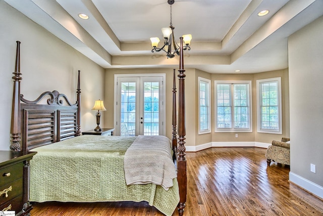 bedroom with french doors, a tray ceiling, dark hardwood / wood-style flooring, and an inviting chandelier