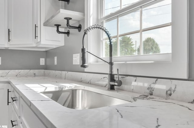 room details with white cabinets, a sink, and light stone countertops