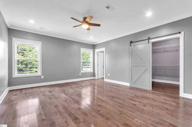 unfurnished bedroom featuring baseboards, visible vents, a barn door, and wood finished floors