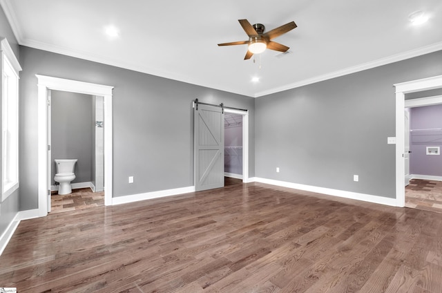 unfurnished bedroom featuring a walk in closet, ornamental molding, baseboards, a barn door, and wood finished floors
