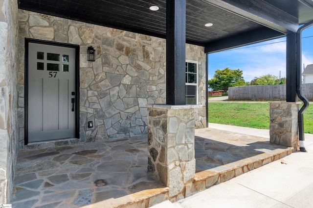 view of exterior entry featuring stone siding, a patio, and fence