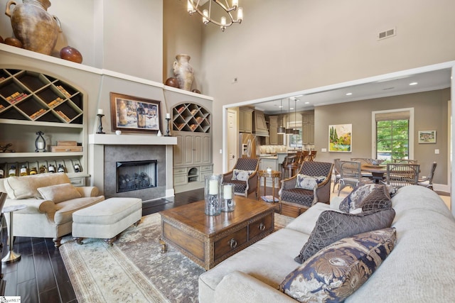 living room with a towering ceiling, an inviting chandelier, a high end fireplace, and hardwood / wood-style flooring