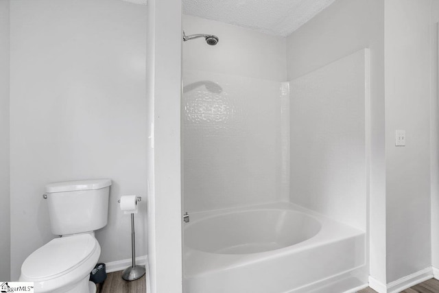 bathroom with wood-type flooring, a textured ceiling, shower / bath combination, and toilet