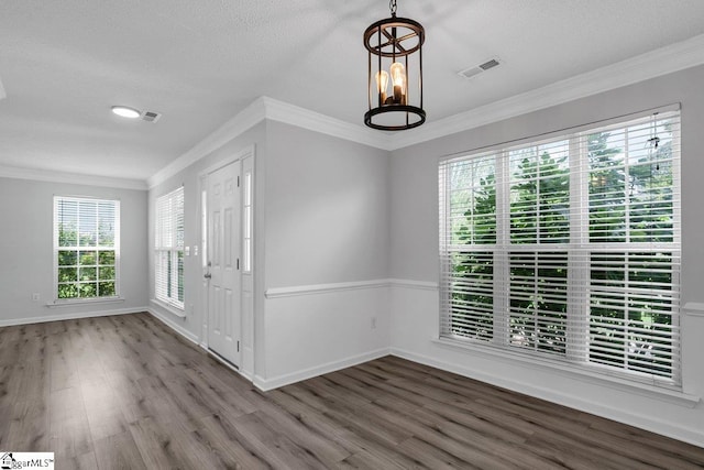 spare room with a textured ceiling, crown molding, wood-type flooring, and a chandelier