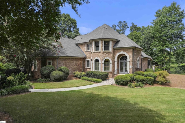 view of front facade with roof with shingles, a front lawn, french doors, and brick siding