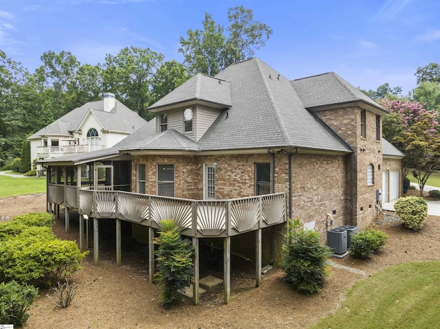 rear view of house featuring roof with shingles, brick siding, a garage, cooling unit, and a wooden deck