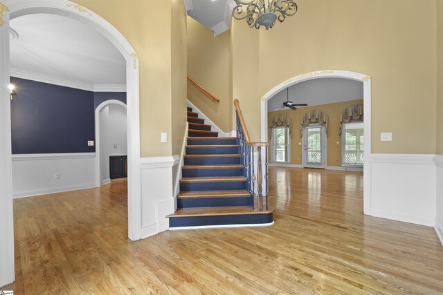 stairs with hardwood / wood-style floors, ceiling fan with notable chandelier, ornamental molding, and a towering ceiling