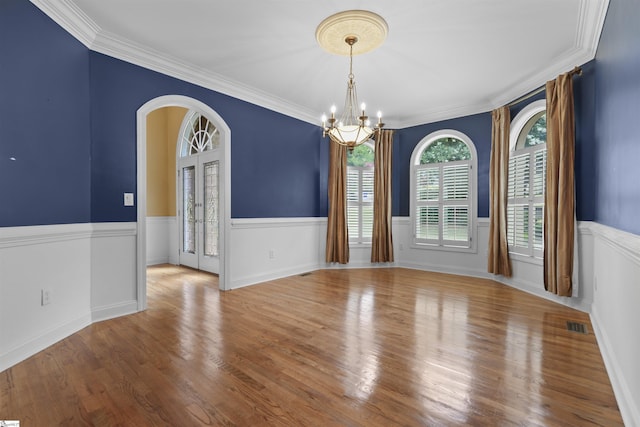 unfurnished room with arched walkways, a notable chandelier, a wainscoted wall, wood finished floors, and crown molding