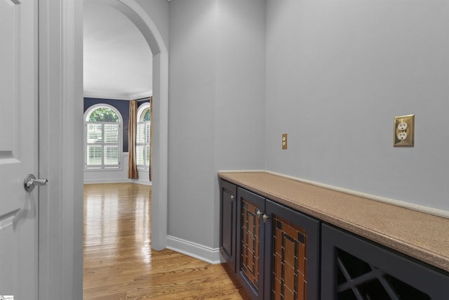 hallway featuring light wood finished floors, baseboards, and arched walkways