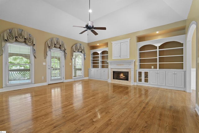 unfurnished living room with built in features, a fireplace, light wood finished floors, vaulted ceiling, and baseboards