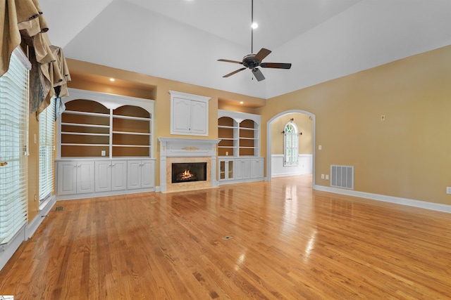 unfurnished living room with built in shelves, a premium fireplace, ceiling fan, and vaulted ceiling