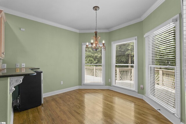 unfurnished dining area featuring wood-type flooring, ornamental molding, and a notable chandelier