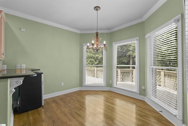 unfurnished dining area featuring an inviting chandelier, baseboards, ornamental molding, and wood finished floors