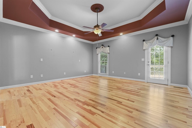 empty room with light wood-type flooring, a raised ceiling, ceiling fan, and crown molding