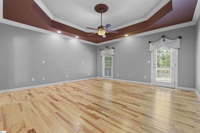 spare room with crown molding, a raised ceiling, ceiling fan, wood finished floors, and baseboards