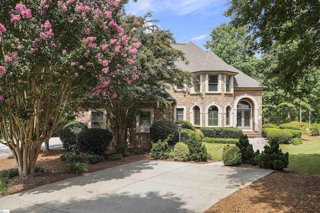 view of front of home featuring french doors, brick siding, a front lawn, and roof with shingles