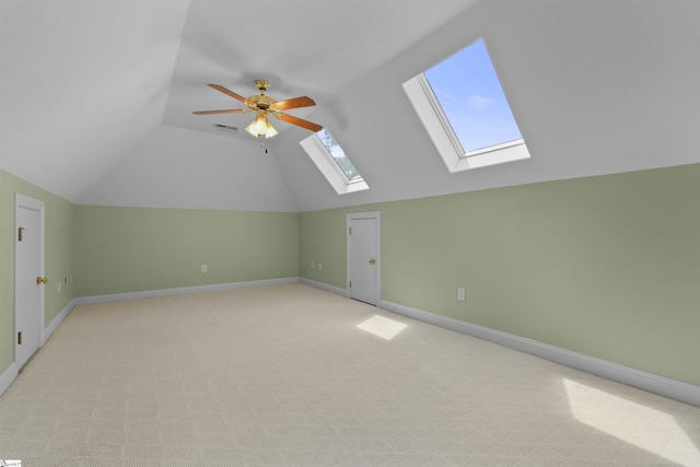 additional living space featuring light colored carpet, visible vents, a ceiling fan, vaulted ceiling with skylight, and baseboards