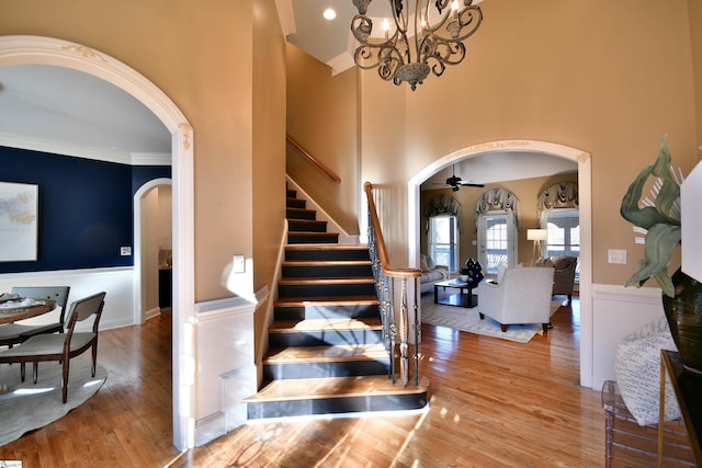 staircase featuring hardwood / wood-style floors, ceiling fan with notable chandelier, and crown molding