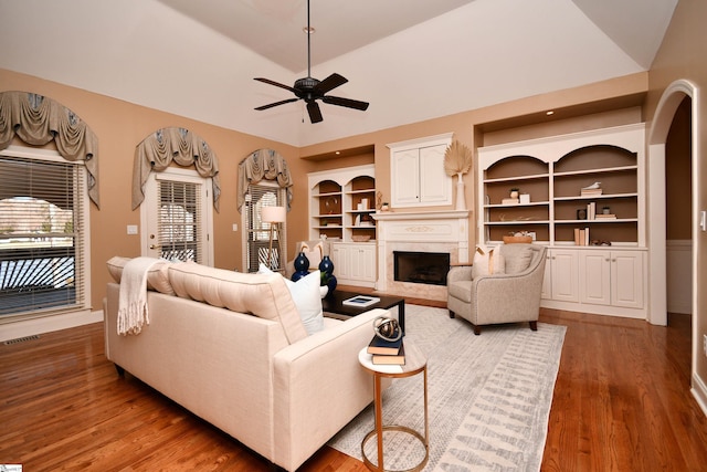 living room featuring ceiling fan, built in features, wood-type flooring, and vaulted ceiling