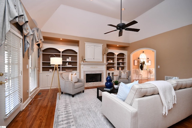 living room with built in shelves, dark hardwood / wood-style floors, ceiling fan, and vaulted ceiling