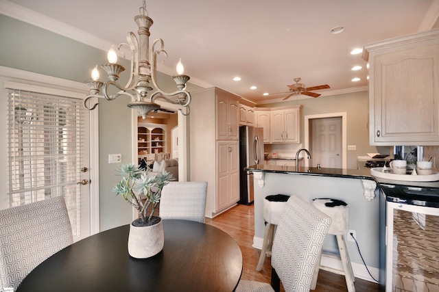 dining room featuring ceiling fan with notable chandelier, sink, crown molding, light wood-type flooring, and beverage cooler