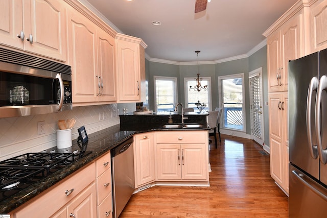 kitchen featuring sink, dark stone counters, pendant lighting, appliances with stainless steel finishes, and light wood-type flooring